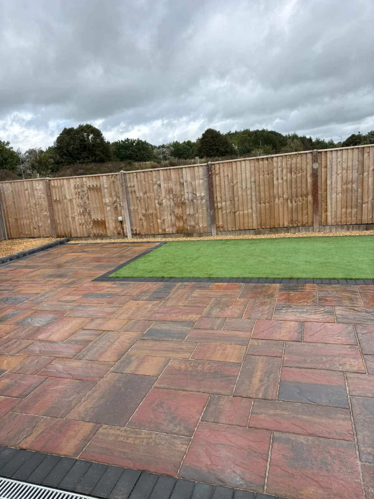 Large sandstone paved garden with artificial grass and timber boundary fencing