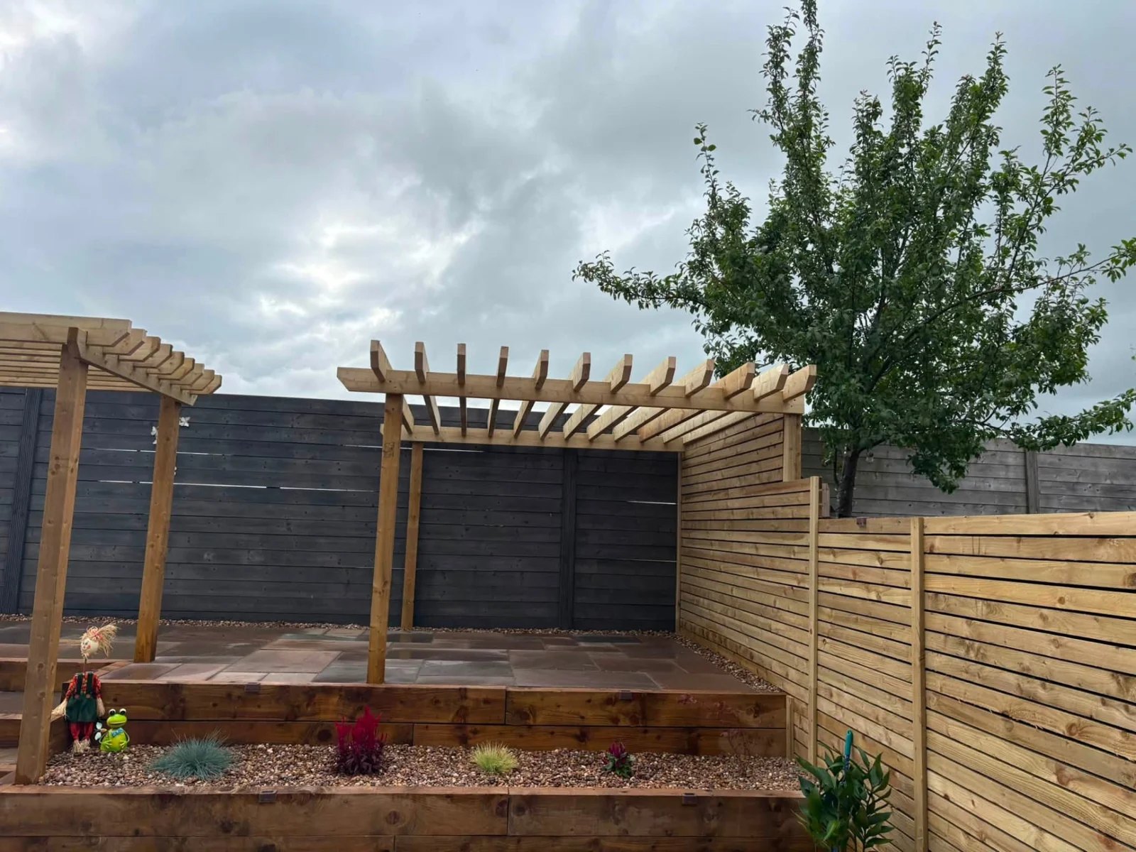 Timber pergola over raised paving with sleeper planting beds and timber screening